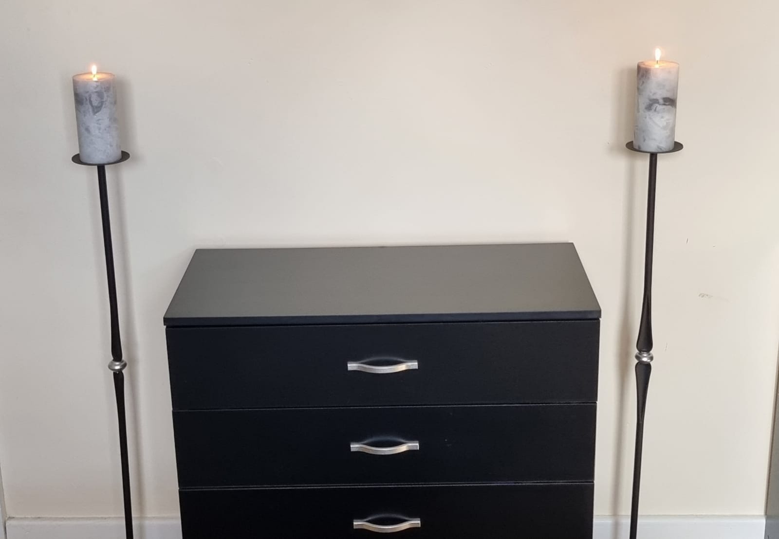Modern floor standing candle holders with candlesticks lit next to a set of drawers